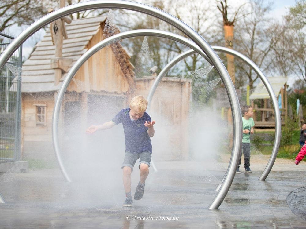Een kind rent door de waternevel van de waterbogen