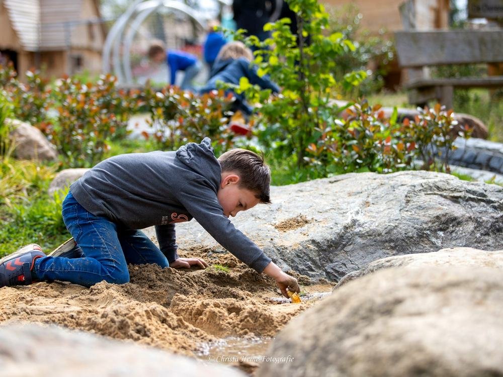 Een kind graaft in het zand van de natuurspeeltuin