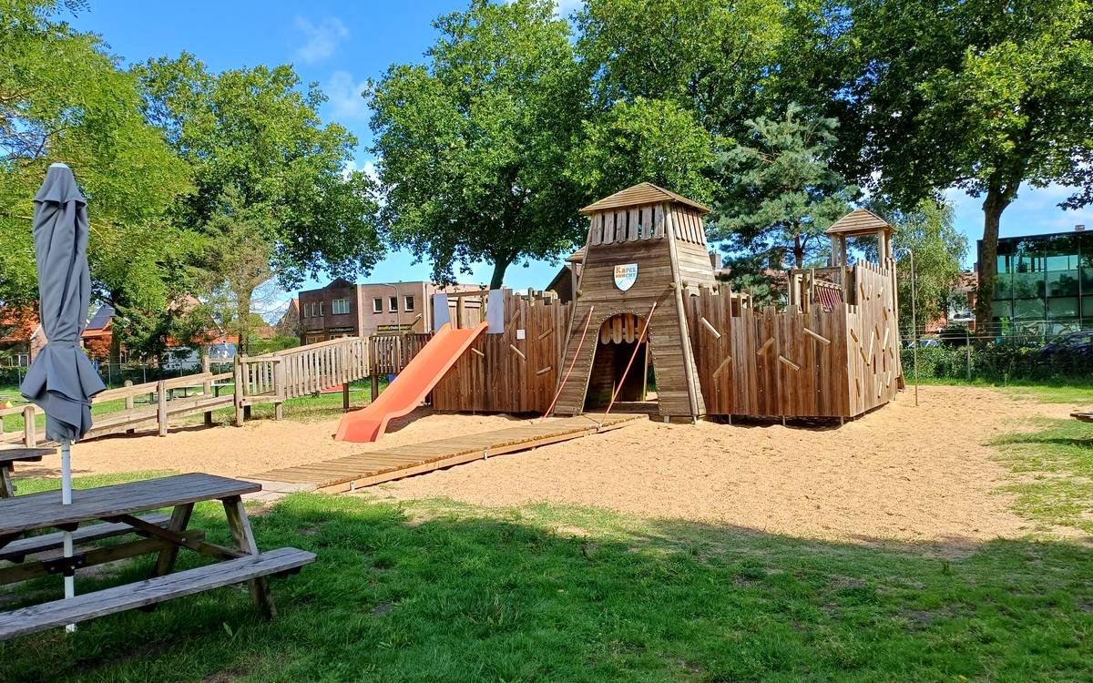 Het houten speelkasteel met glijbaan en zandvlakte